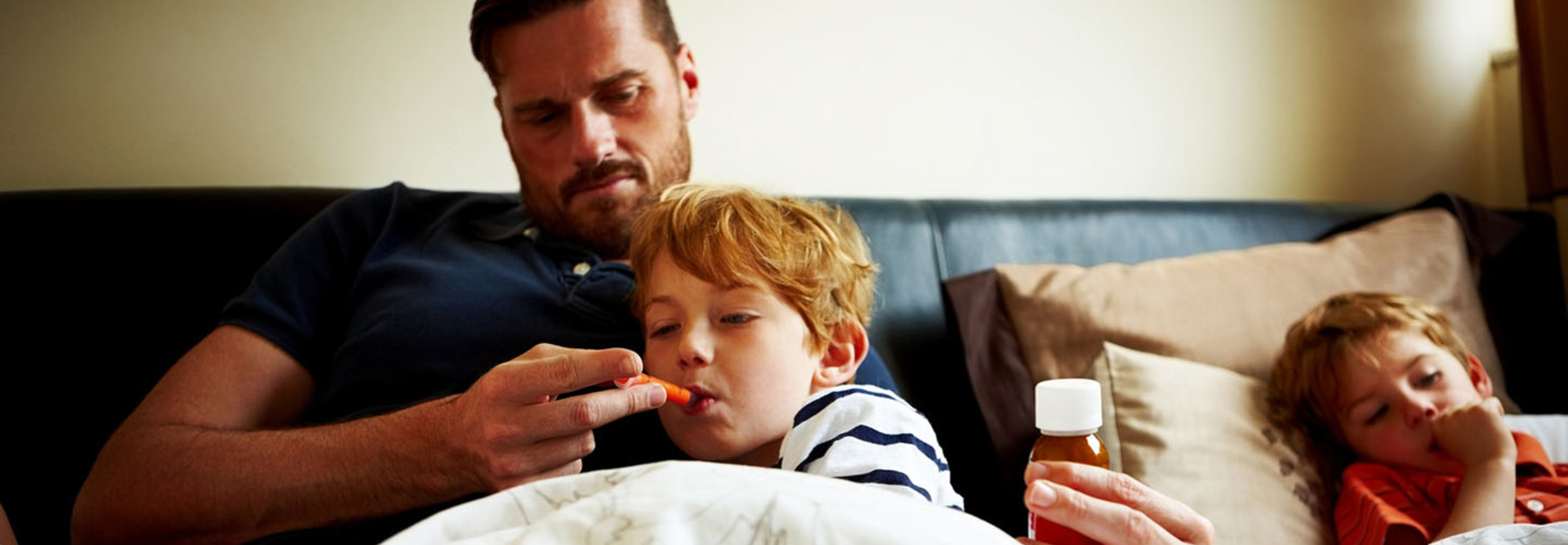 Father measuring temperature of his sick son, while lying on bed