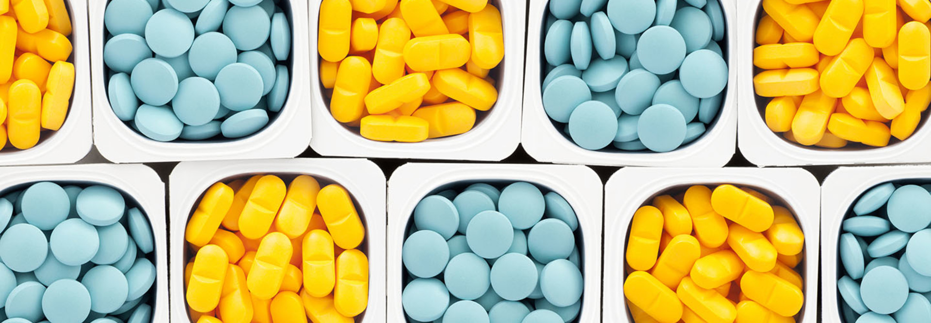 Top view of lots of pills held in plastic containers in a crisscross pattern