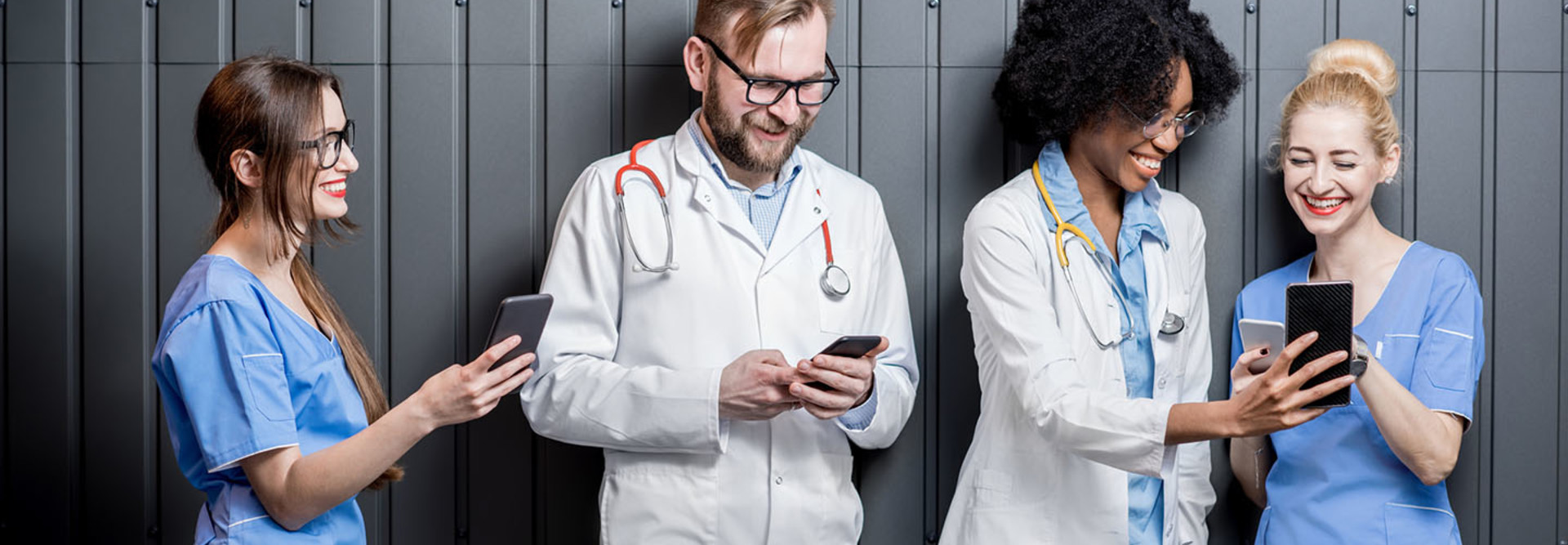 Multi ethnic group of medics standing with phones on the gray wall background