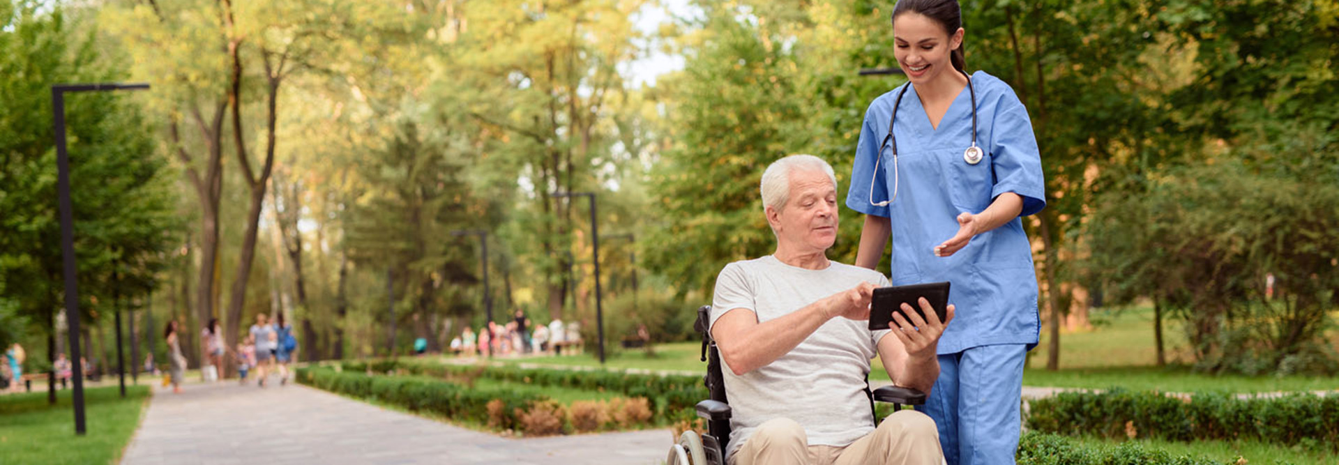An old man sitting in a wheelchair shows the nurse something on his tablet