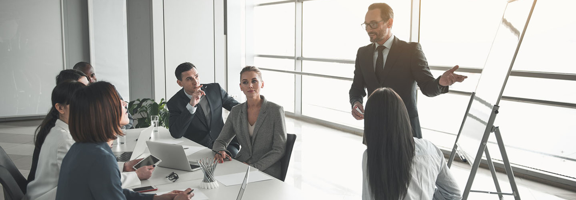 Elegant man standing in front of coworkers near marker board and indicating at it while speaking
