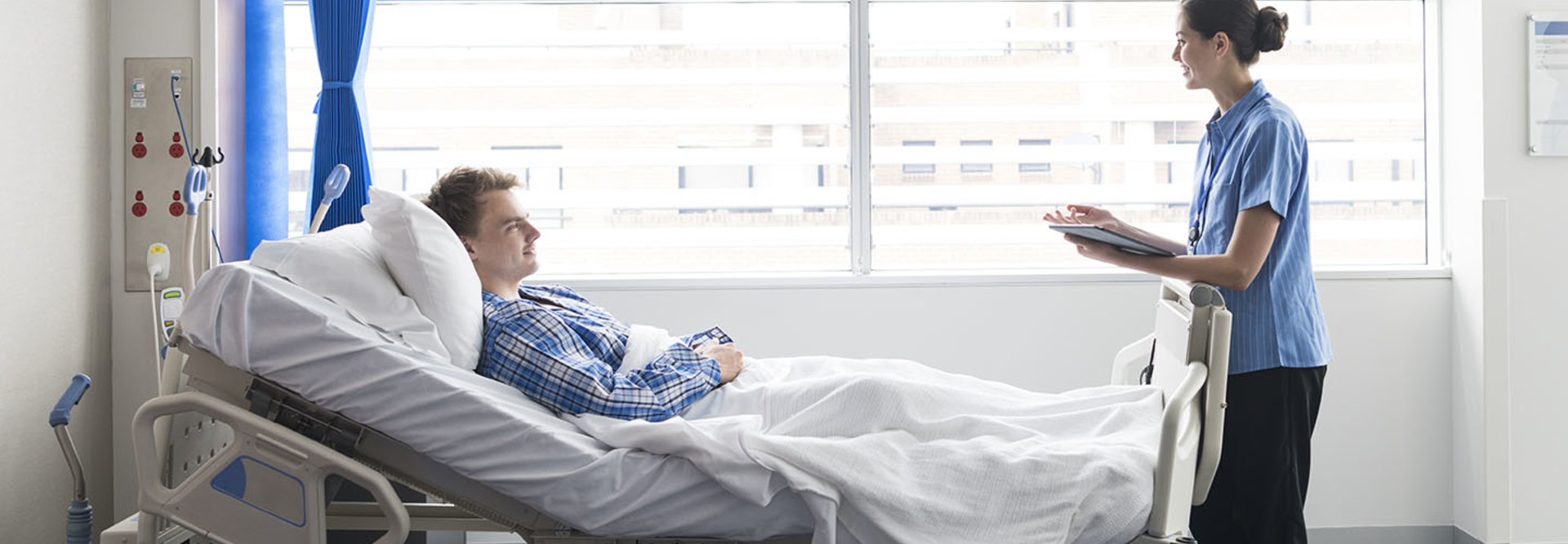 Young man lying in bed in hospital with female nurse
