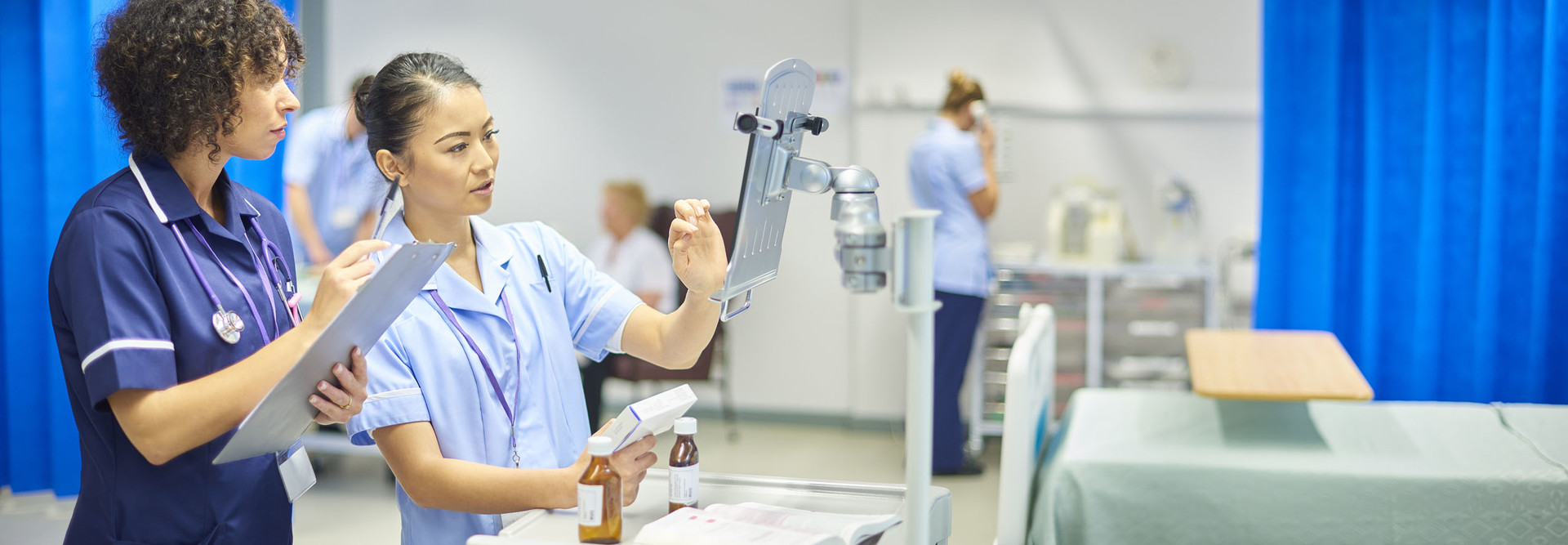 a young nurse checks the dosage on her digital tablet supervised by her staff nurse
