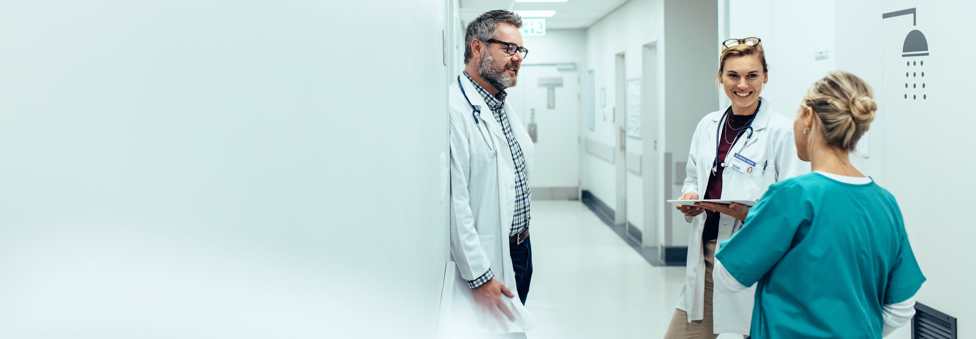 Medical team discussing in corridor at hospital. Mature doctor discussing with coworkers while standing in hospital hallway.