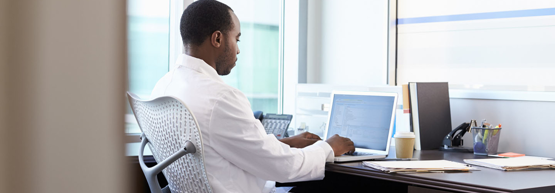 Doctor Wearing White Coat Working On Laptop In Office