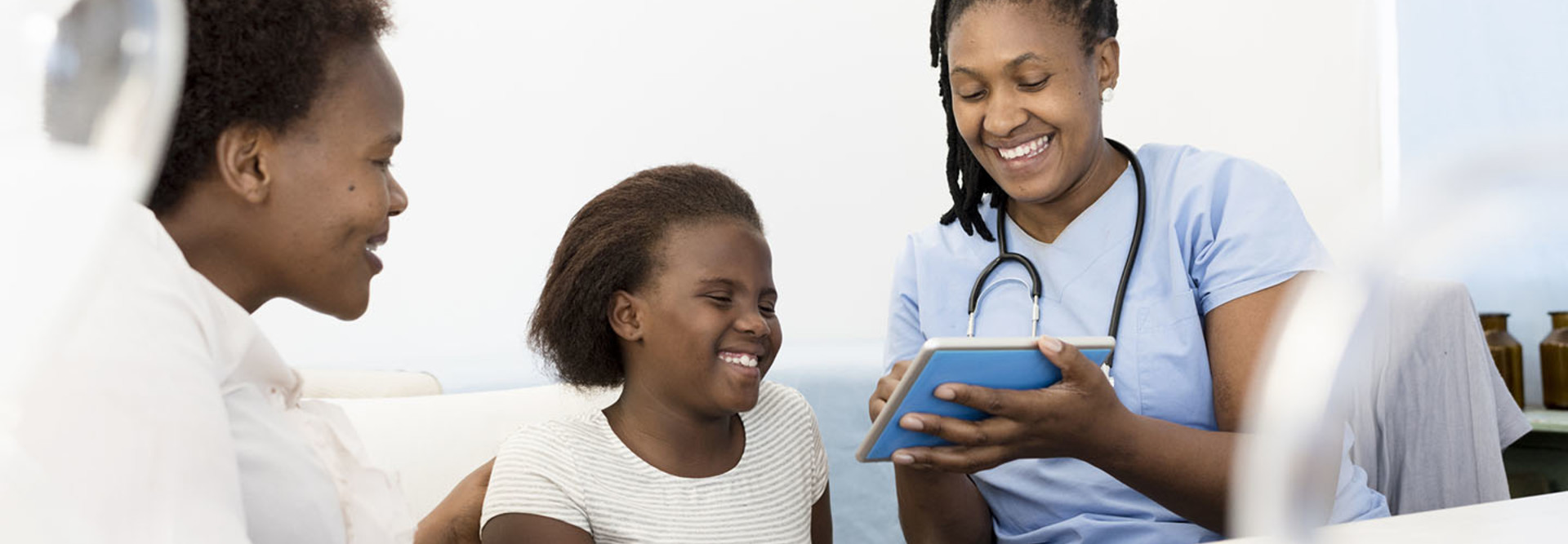 Female Doctor explaining test results on a digital tablet to a Mother & child in her consultation room at daytime.