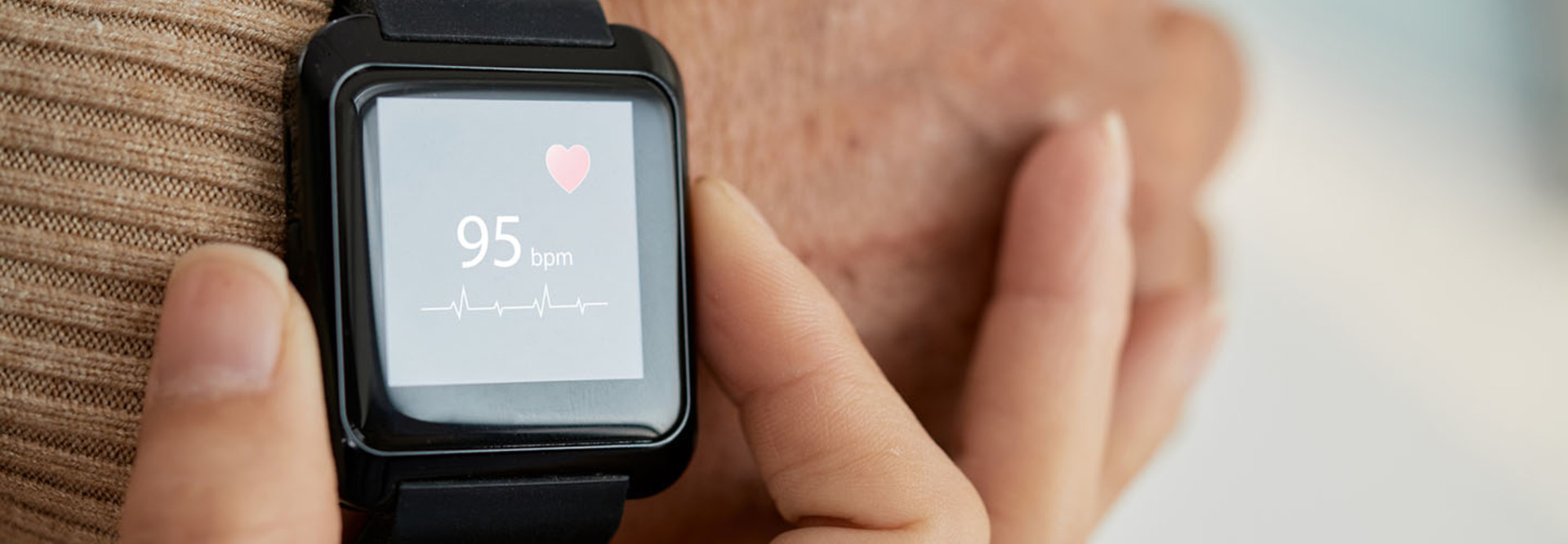 Close-up shot of unrecognizable doctor checking pulse of her senior patient with help of smart watch, blurred background