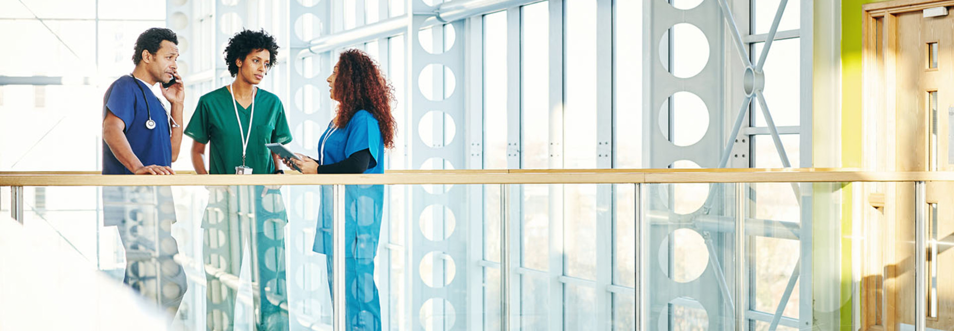 Three diverse medical professionals talking in modern hospital corridor