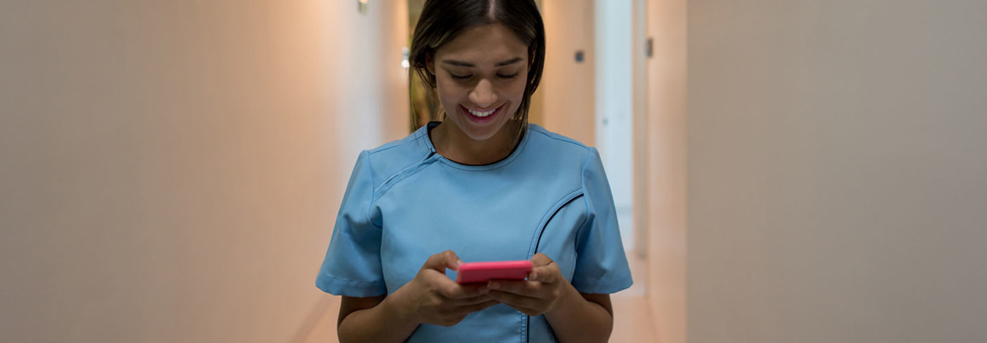 Latin american nurse walking through the hospital's corridor chatting on her smartphone smiling very happy