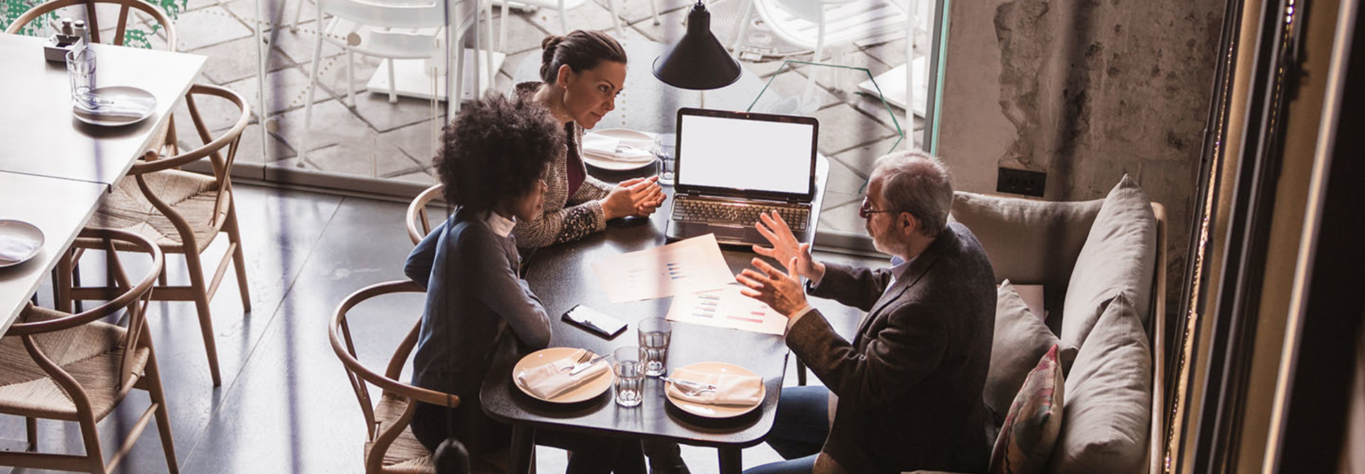 Two female collegues having business meeting in high end restaurant with senior client. Multi-ethnic group. High angle view