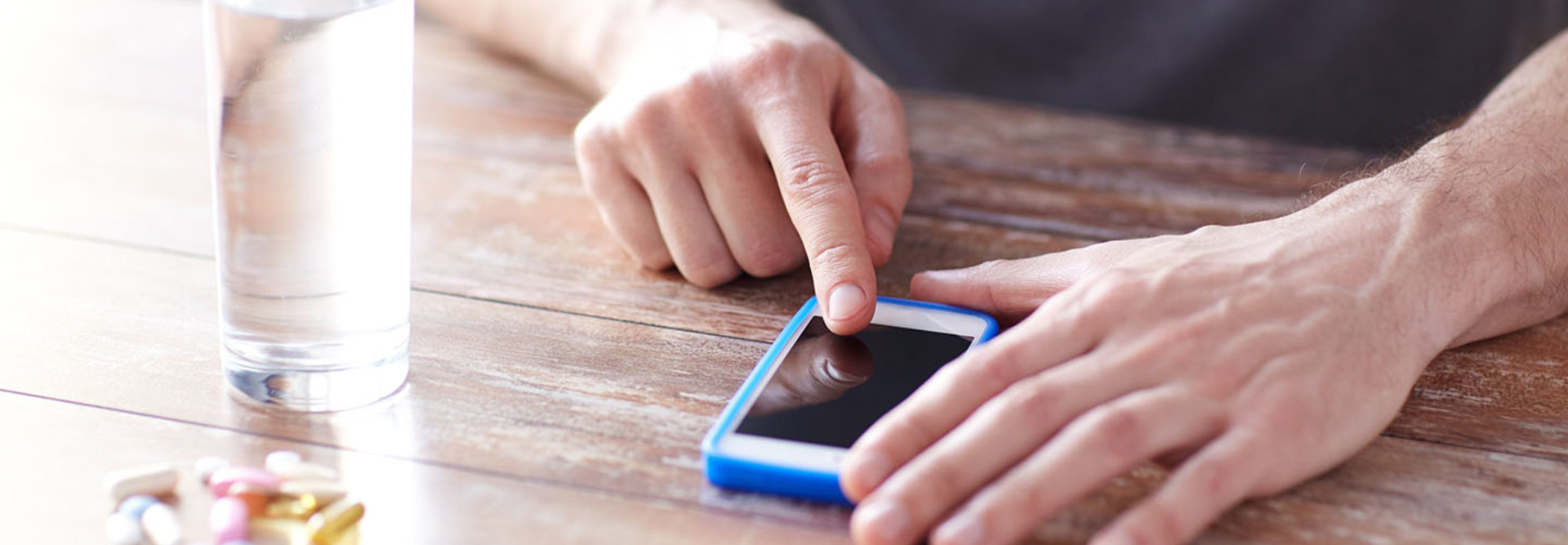 A man gets a medication reminder on his smartphone. There are pills and a glass of water on the table.