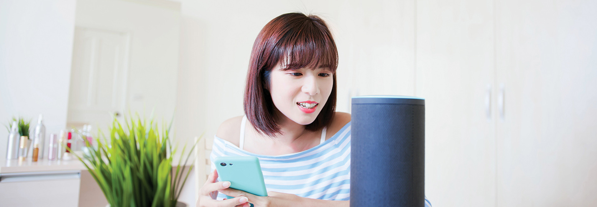 Woman with phone in hand speaking to a voice device.