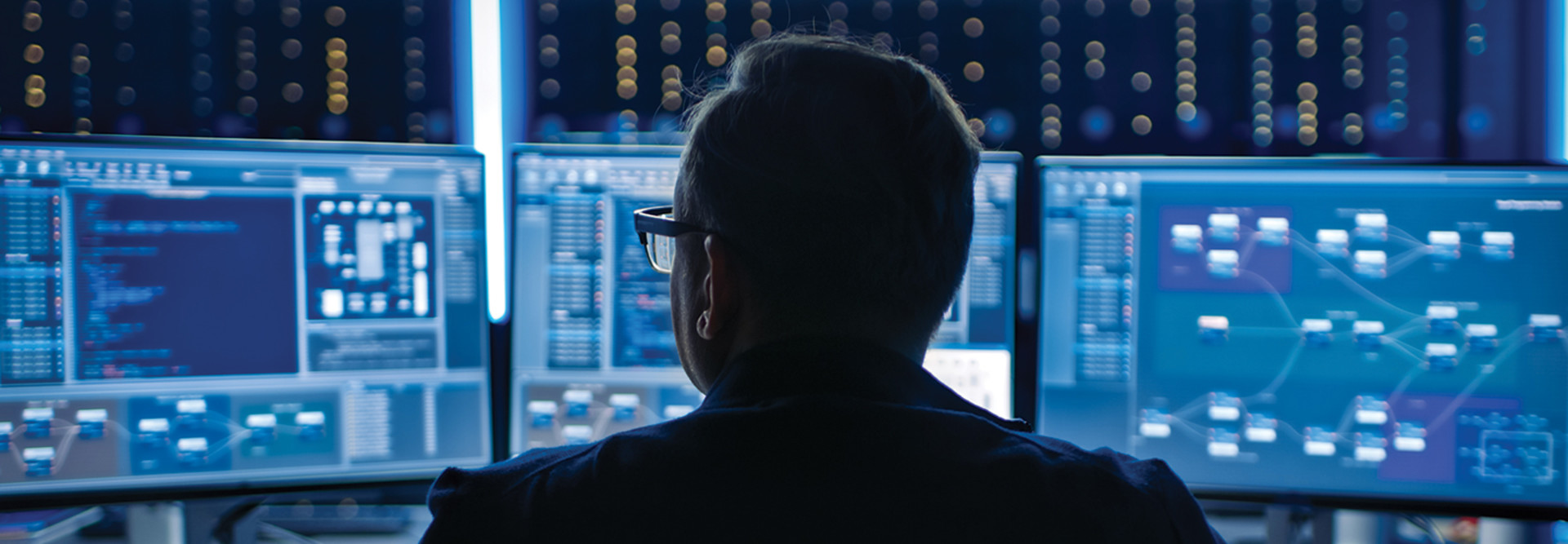 Man at desk looking at 3 computer monitors.
