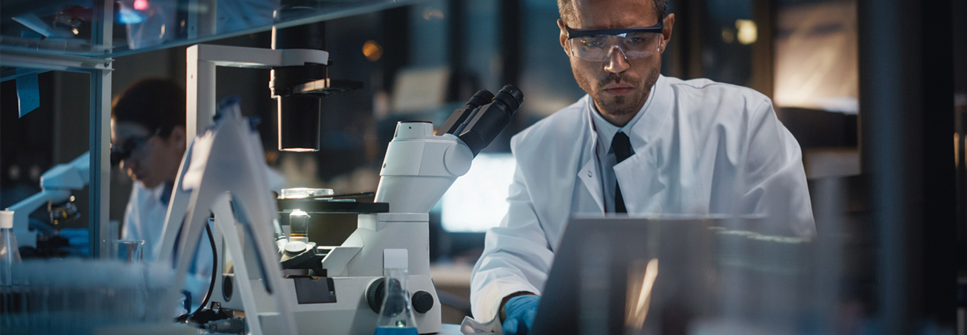 Female doctor looking through microscope, male doctor on computer