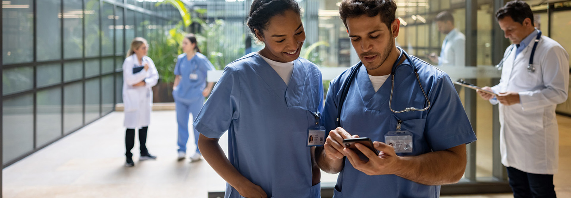 two nurses look at cell phone in hospital lobby