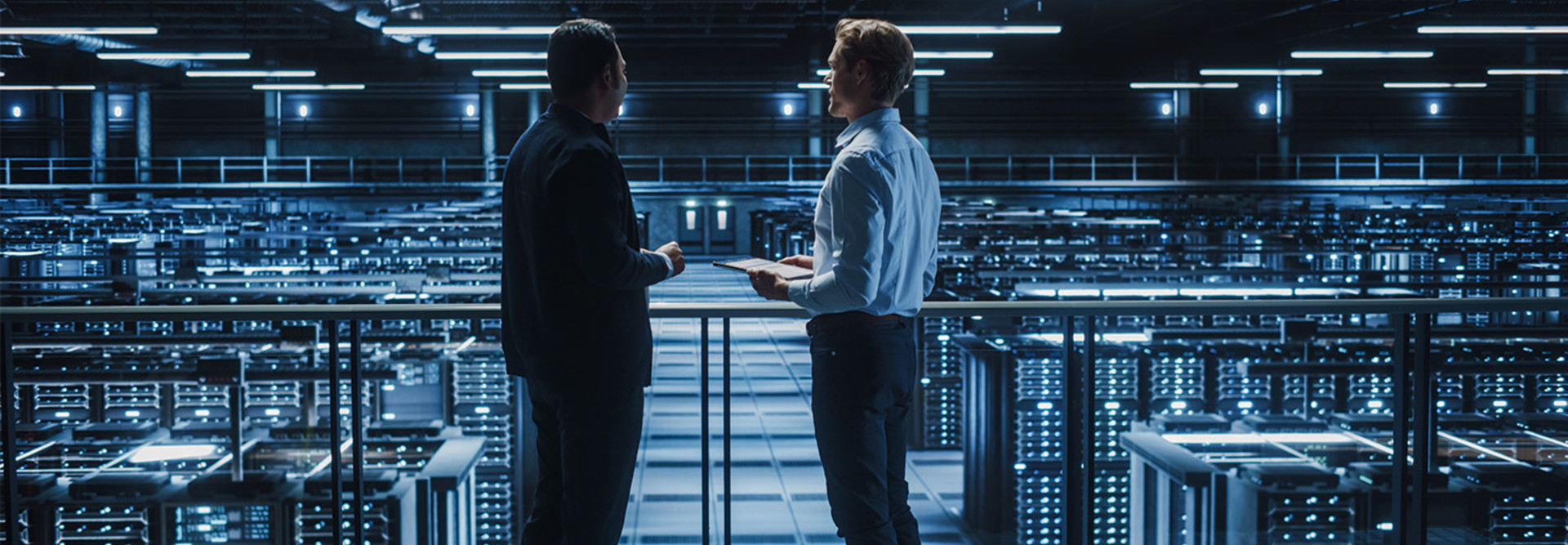 two IT professionals stand over server room