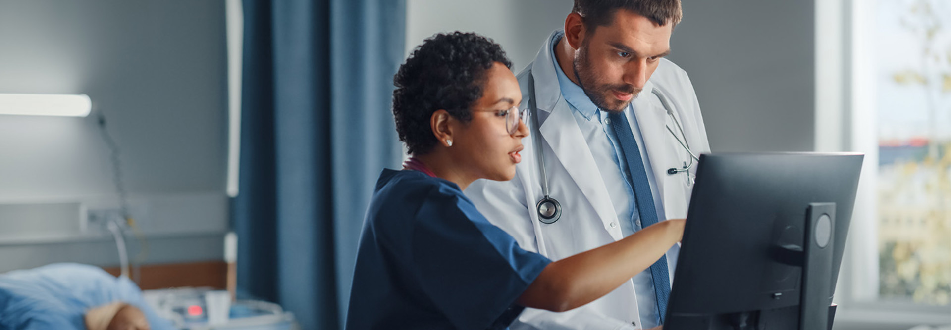 nurse and physician collaborate over desktop computer in patient room