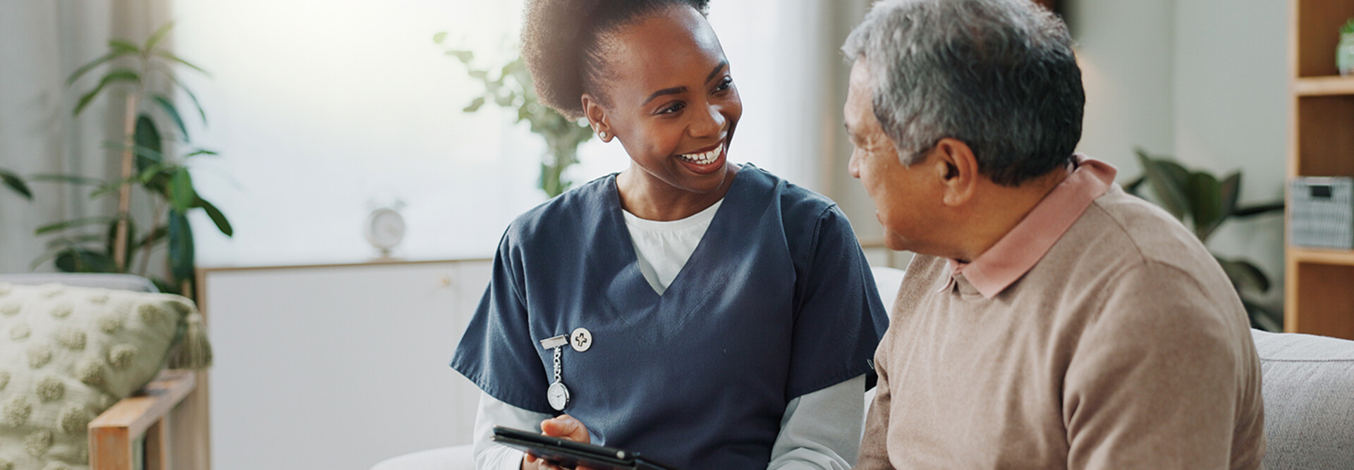 nurse and older adult talk on couch with tablet