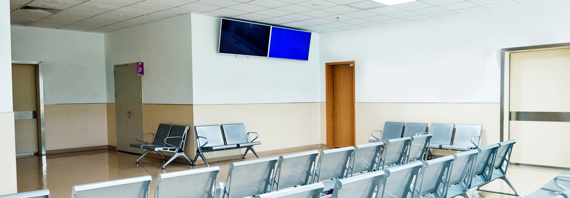 Empty seats in hospital waiting room with a television monitor.