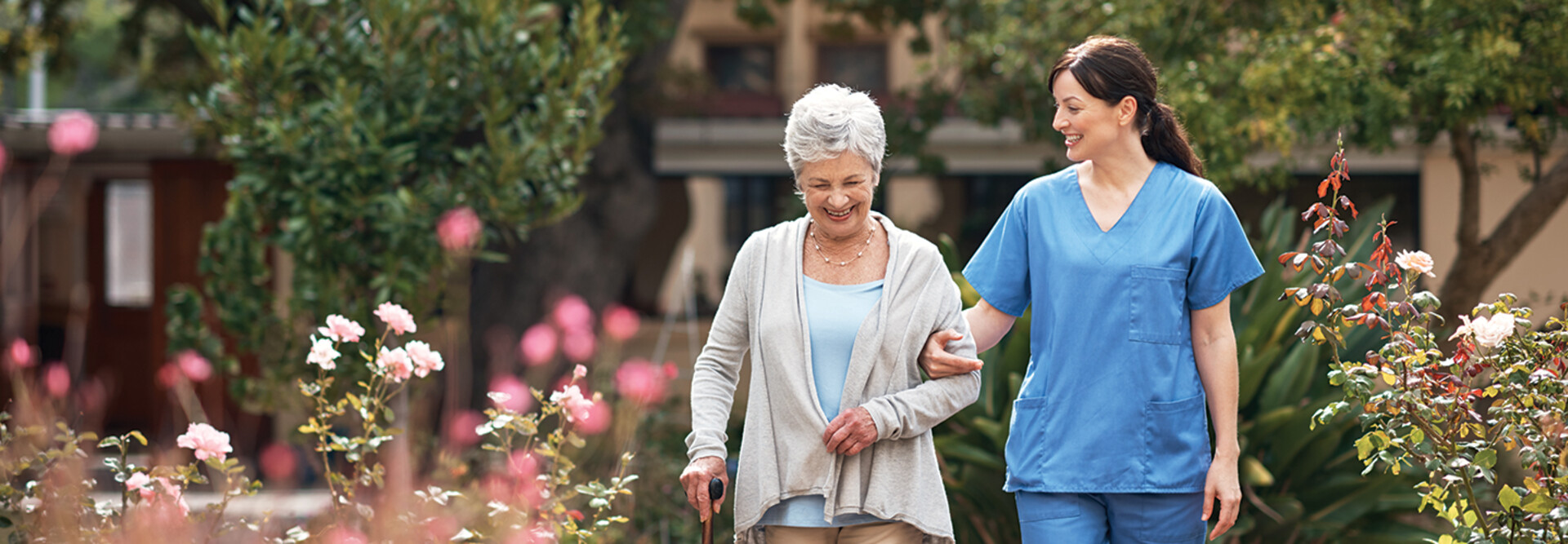 nurse walks with senior woman through a garden