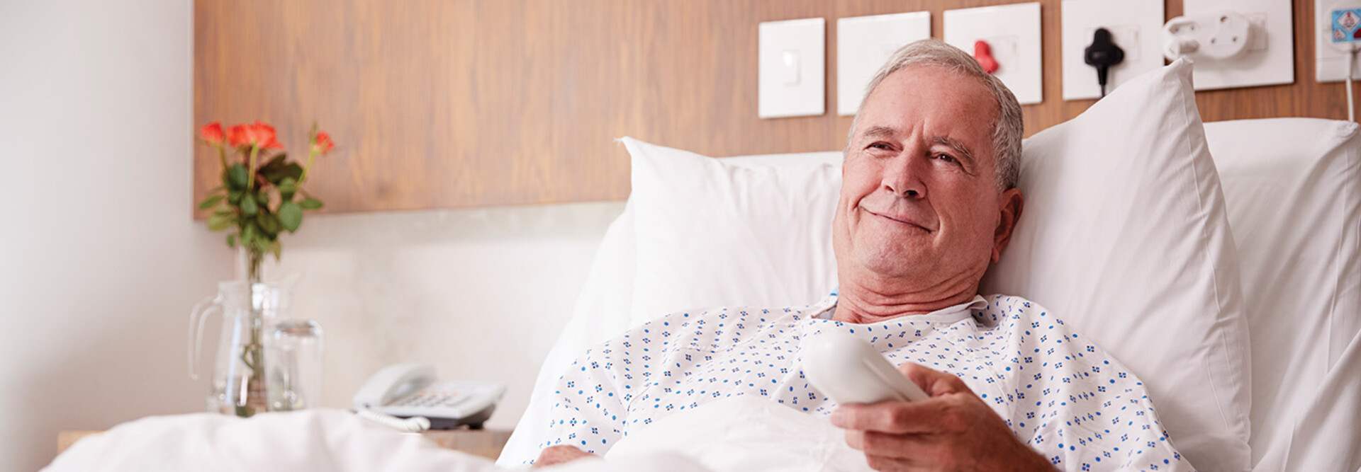 man in hospital bed uses remote to watch tv