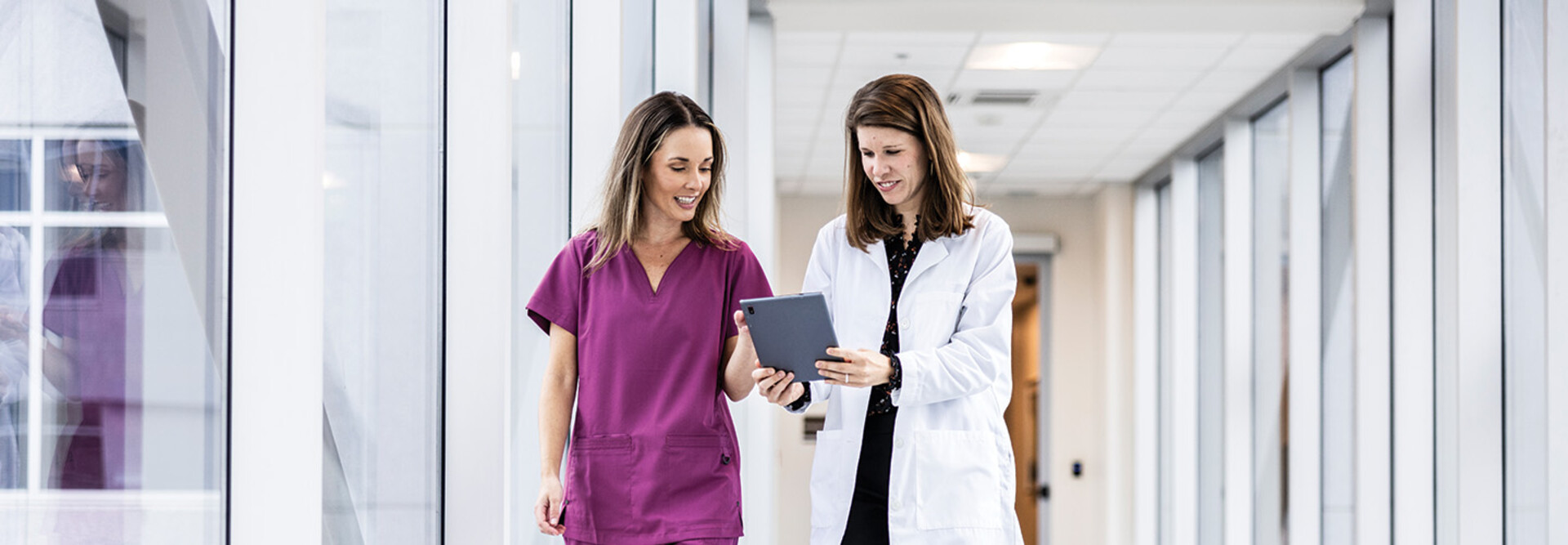 two clinicians walking down hallway looking at a tablet