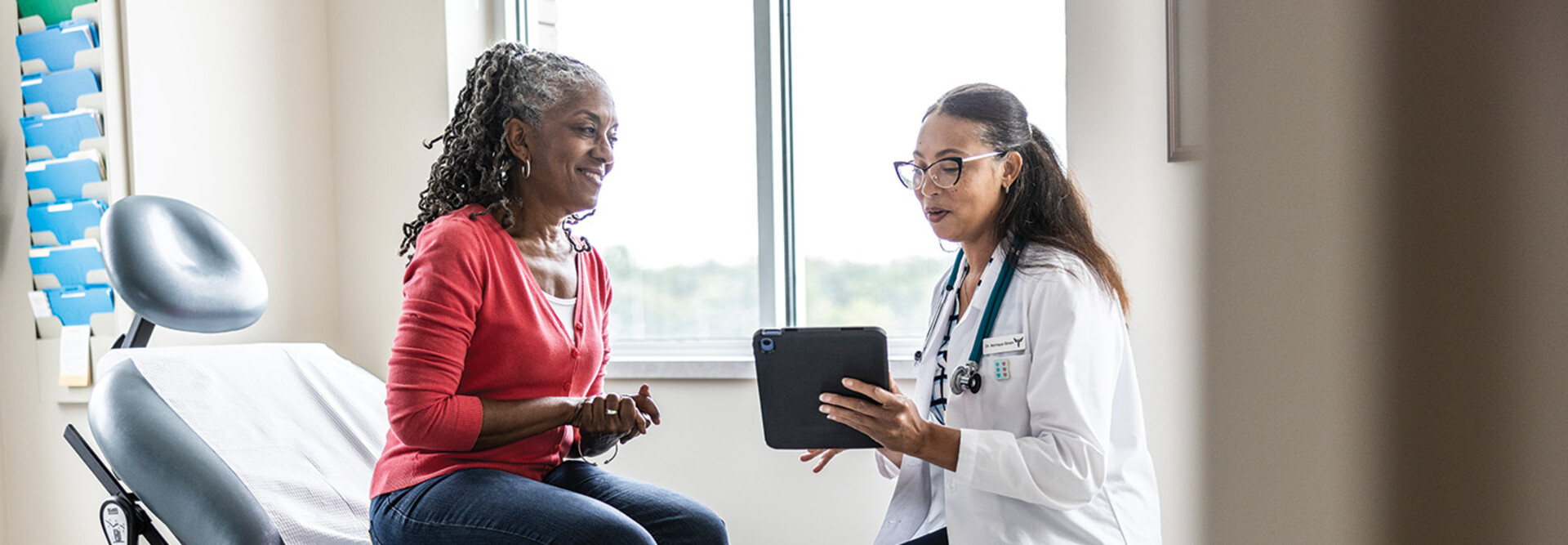 doctor talks to patient in exam room while holding a tablet