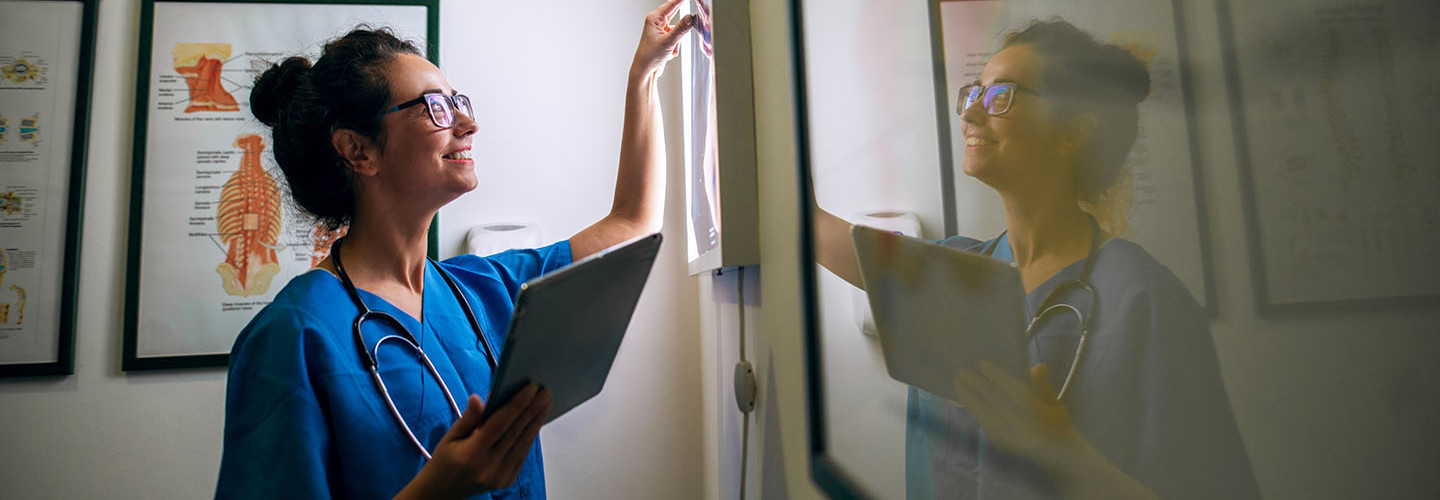 Side view of smiling middle aged nurse checking X-ray in a doctors office.