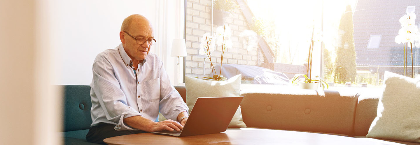 Senior man works with laptop as sun shines through windows