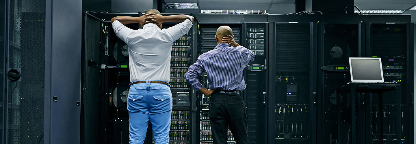 Rearview shot of two IT technicians having difficulty repairing a computer in a data center
