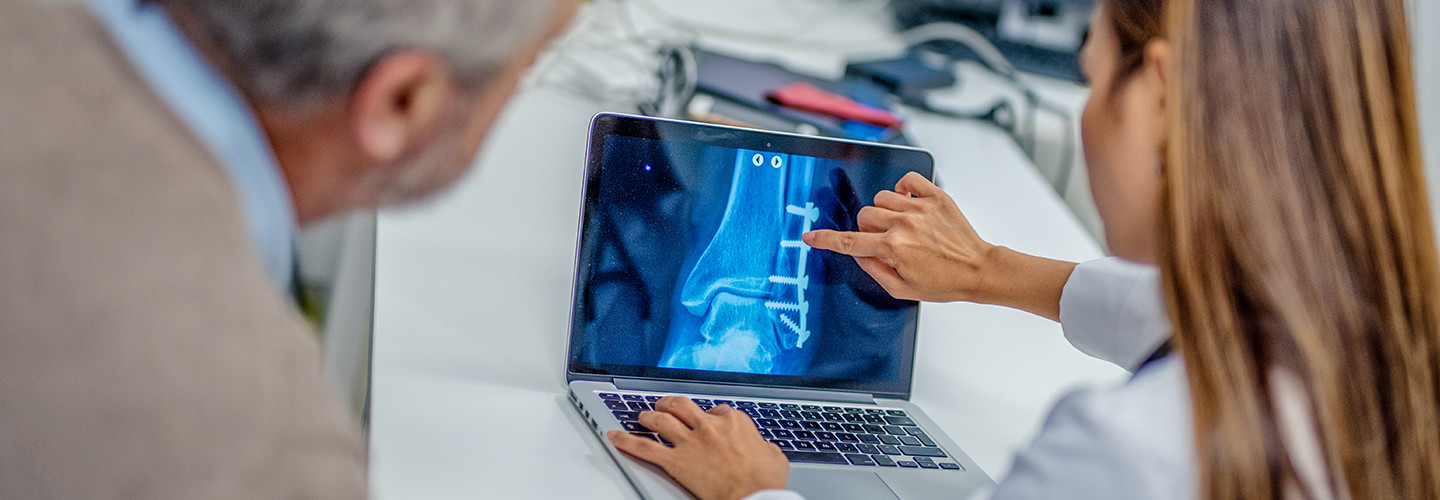 Doctor showing her patient’s knee reconstruction after surgery on a laptop in her office.
