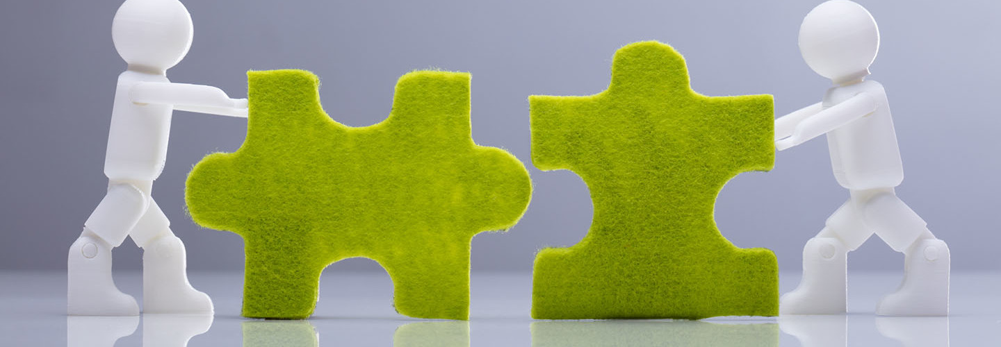 Side View Of Two Miniature Human Figures Solving Green Jigsaw Puzzles On Grey Background