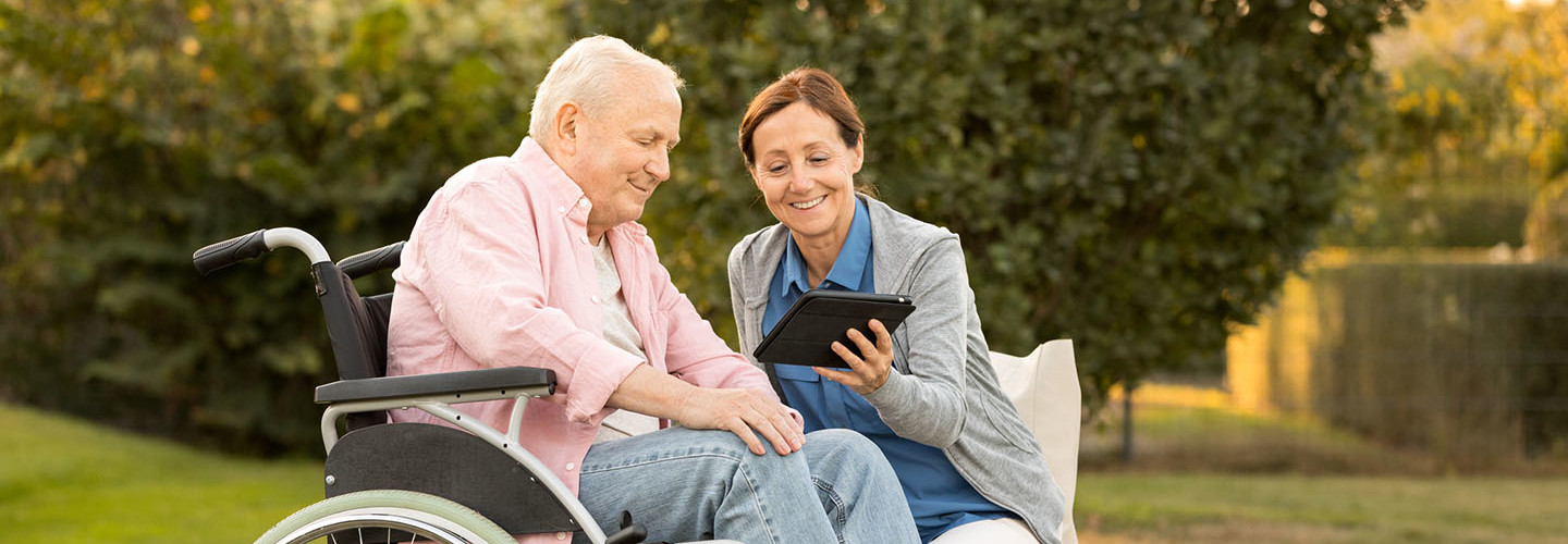 Caregiver and senior man on park bench, using digital tablet