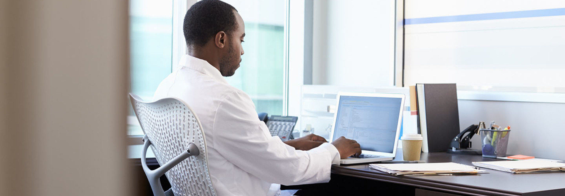 Doctor Wearing White Coat Working On Laptop In Office