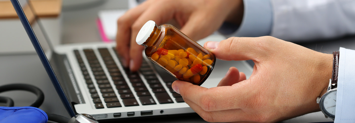 Male medicine doctor hands hold jar of pills and type something on laptop computer keyboard.