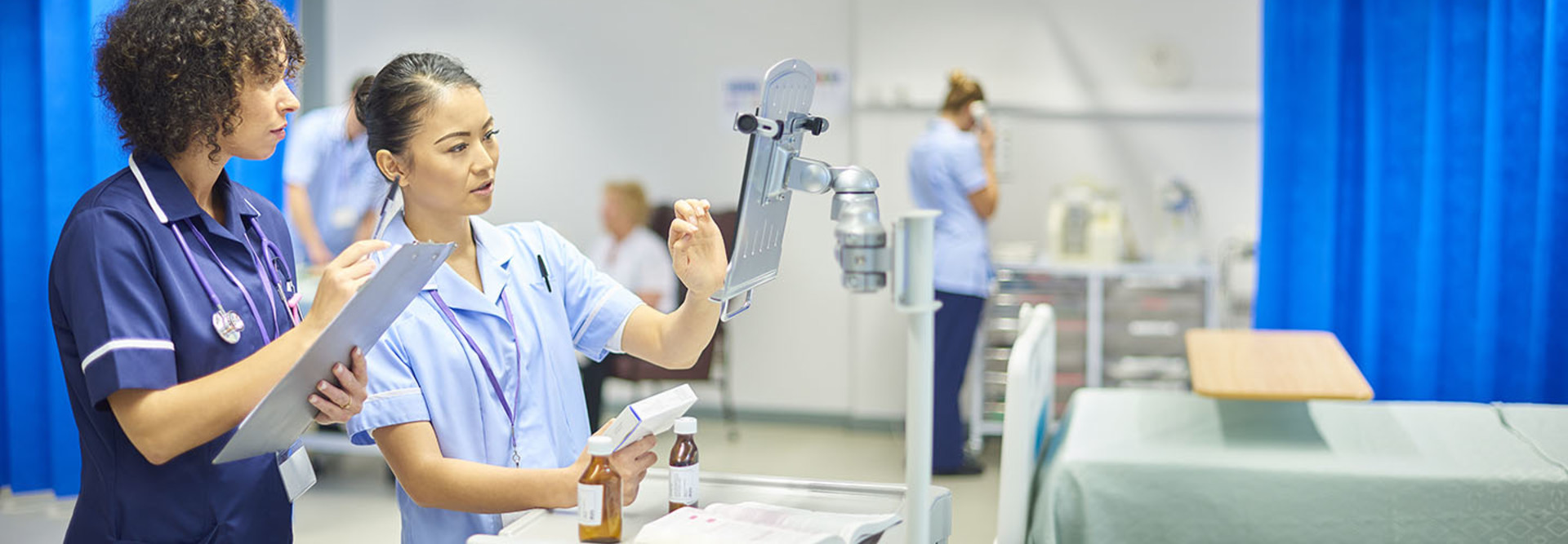 A young nurse checks the dosage on her digital tablet supervised by her staff nurse.