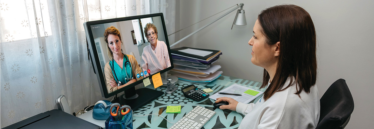 Doctor at desk speaking with patient through video conference.