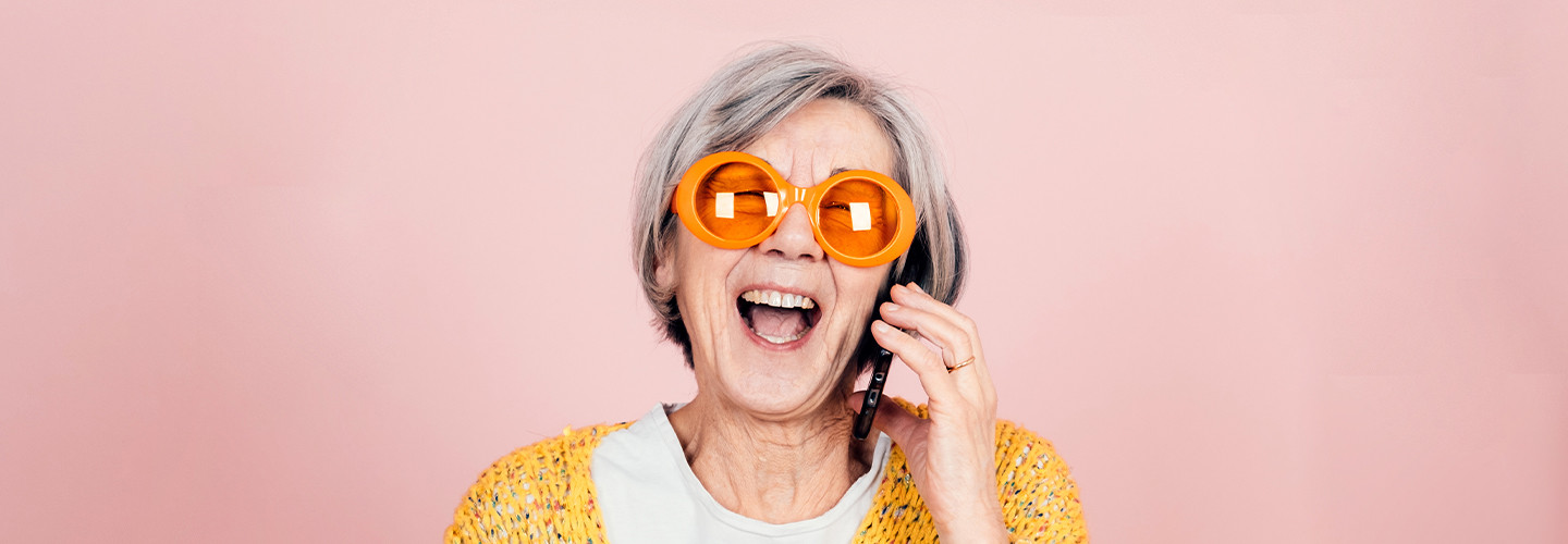 older adult woman wearing sunglasses laughs while on a smart phone