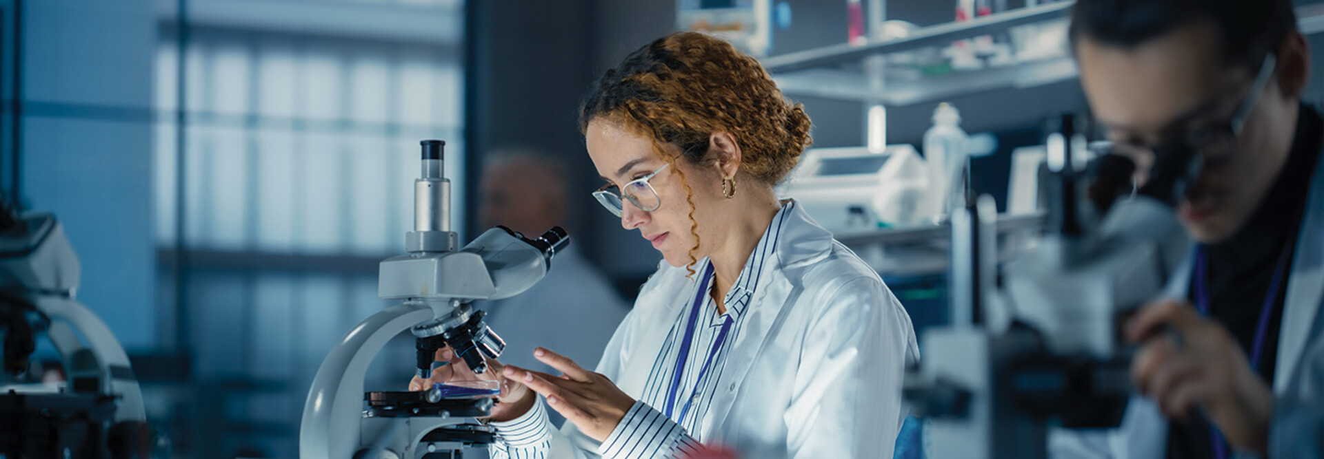 healthcare researcher looks through microscope in dark lab