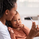 mother takes baby's temperature on telehealth call with doctor