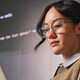woman wearing glass holds laptop in front of wall of code