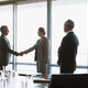 business people gather around conference table as leaders shake hands