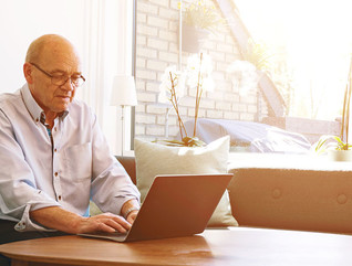 Senior man works with laptop as sun shines through windows