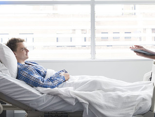 Young man lying in bed in hospital with female nurse