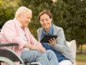 Caregiver and senior man on park bench, using digital tablet