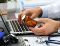 Male medicine doctor hands hold jar of pills and type something on laptop computer keyboard.