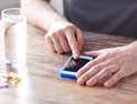 A man gets a medication reminder on his smartphone. There are pills and a glass of water on the table.