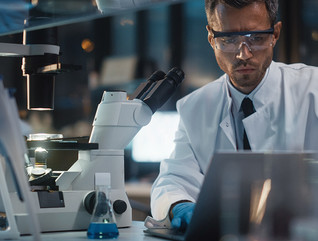 Female doctor looking through microscope, male doctor on computer