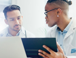 two doctors discuss treatment plans over laptop and tablet