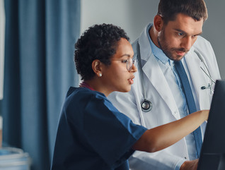 nurse and physician collaborate over desktop computer in patient room
